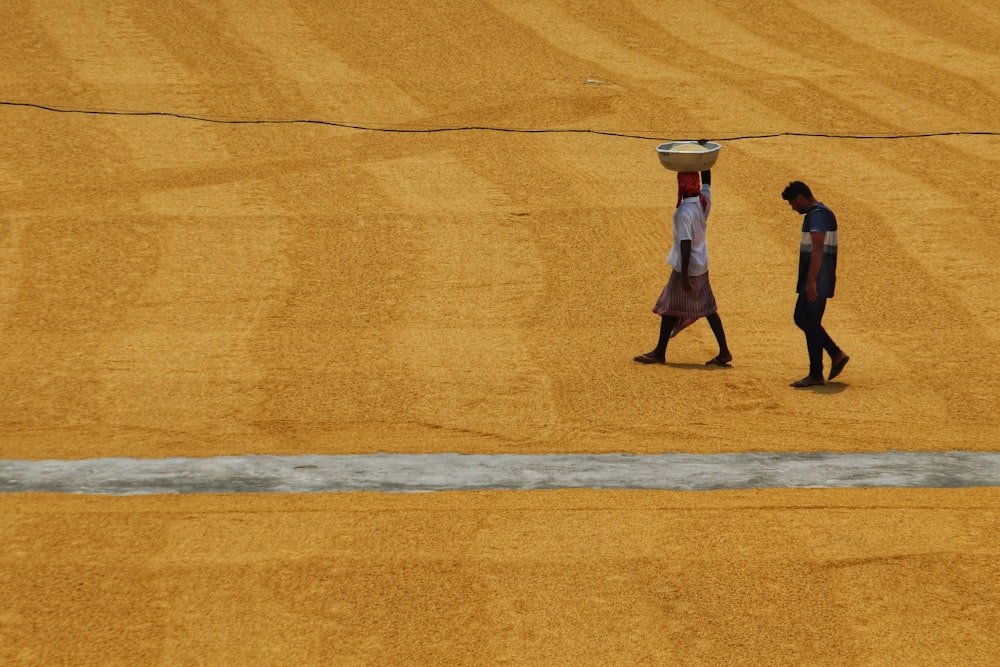 two men walking across a field with a basket on their head