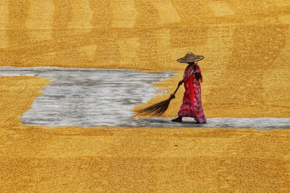 a woman in a red dress and straw hat with a broom
