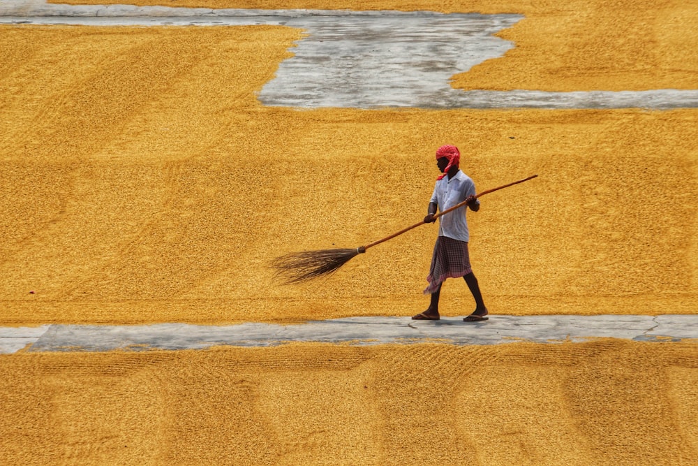 a man with a broom walks through a field of grain