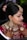 A woman is adorned in traditional bridal attire, featuring intricate jewelry such as a heavy necklace, large earrings, and a forehead ornament known as a maang tikka. Her hair is styled in an updo with decorative flowers. Her hands are beautifully decorated with henna designs. The makeup is elaborate, highlighting her eyes and lips.