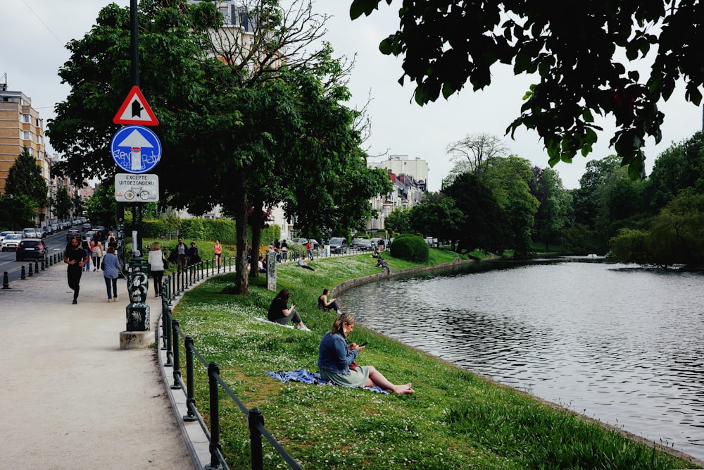 a woman sitting on the grass next to a river