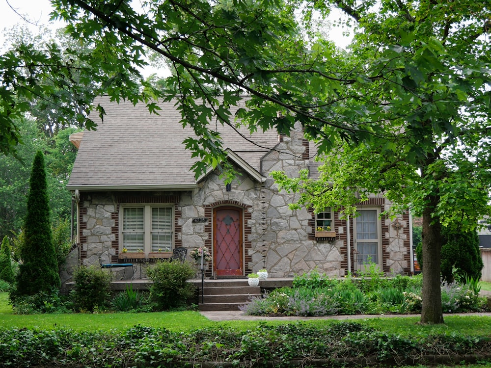 a stone house with a red door surrounded by trees