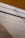 A wall surfaces composed of horizontal tiles with a light beige color dominates the lower portion of the image. The top portion features a section of yellow wood planks on a ceiling with black lines accentuating the divisions. A glass panel or glazed section with condensation is visible between the ceiling and wall.