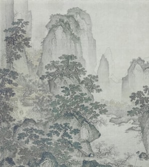 A traditional Chinese landscape painting depicting towering, rugged mountains shrouded in mist. Pine trees are scattered among the rocky terrain, and there appear to be small buildings or pavilions nestled in the forested areas. The scene conveys a sense of peace and solitude.