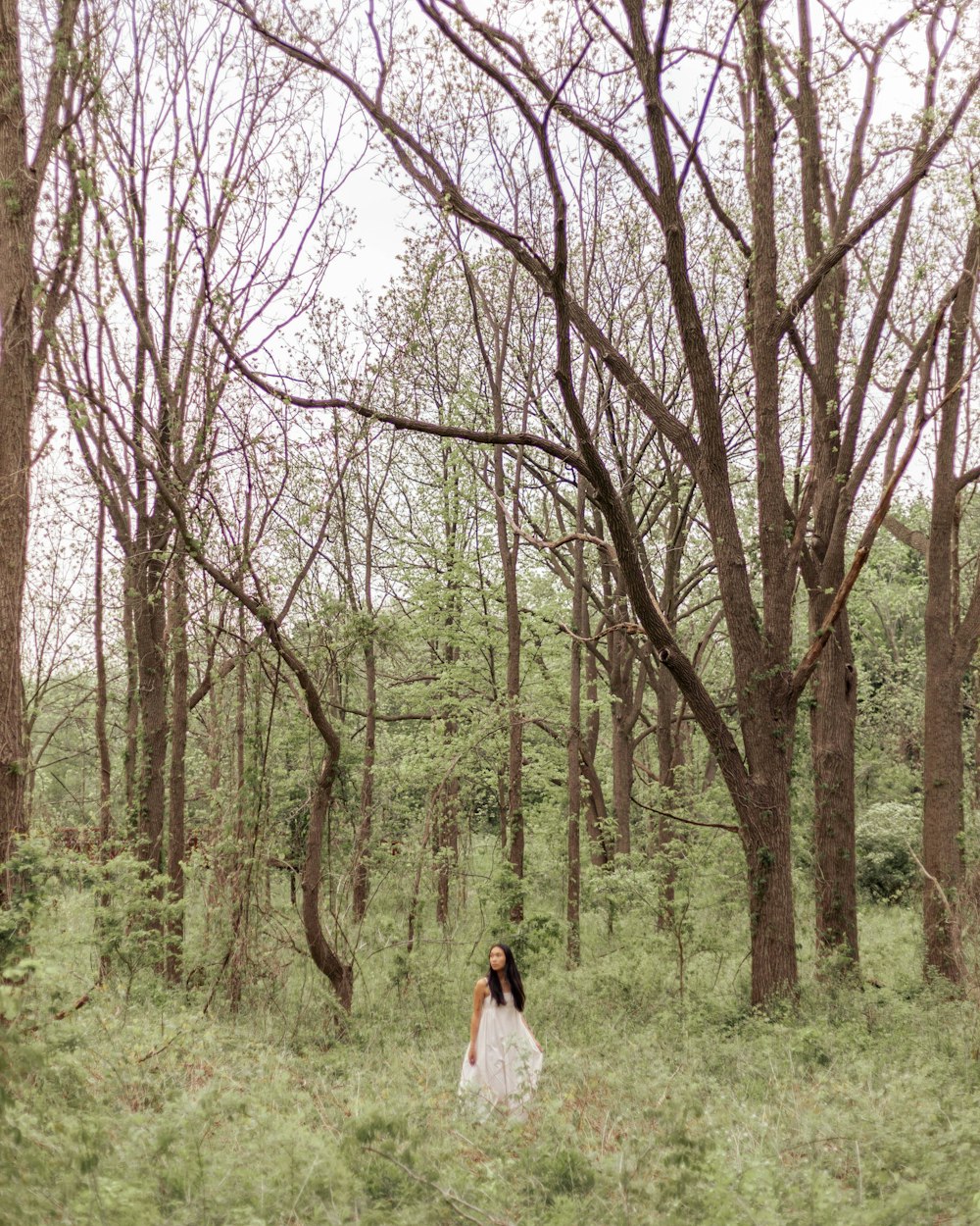 a woman in a white dress walking through a forest