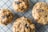 Four oatmeal raisin cookies are placed on a wire cooling rack. The cookies have a rough, crumbly texture with visible oats and dark raisins throughout the surface.