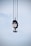 A large industrial crane hook is suspended in the air, hanging from several thick cables. The hook block features a pattern of diagonal red and white stripes. The background is a pale blue sky.