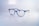 A pair of stylish, blue-rimmed glasses with transparent lenses is placed on a reflective white surface. The brand name 'Esprit' is printed on one of the lenses, along with the words 'Small collection'. The glasses' design is modern and sleek, with a lightweight frame.