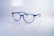 A pair of stylish, blue-rimmed glasses with transparent lenses is placed on a reflective white surface. The brand name 'Esprit' is printed on one of the lenses, along with the words 'Small collection'. The glasses' design is modern and sleek, with a lightweight frame.