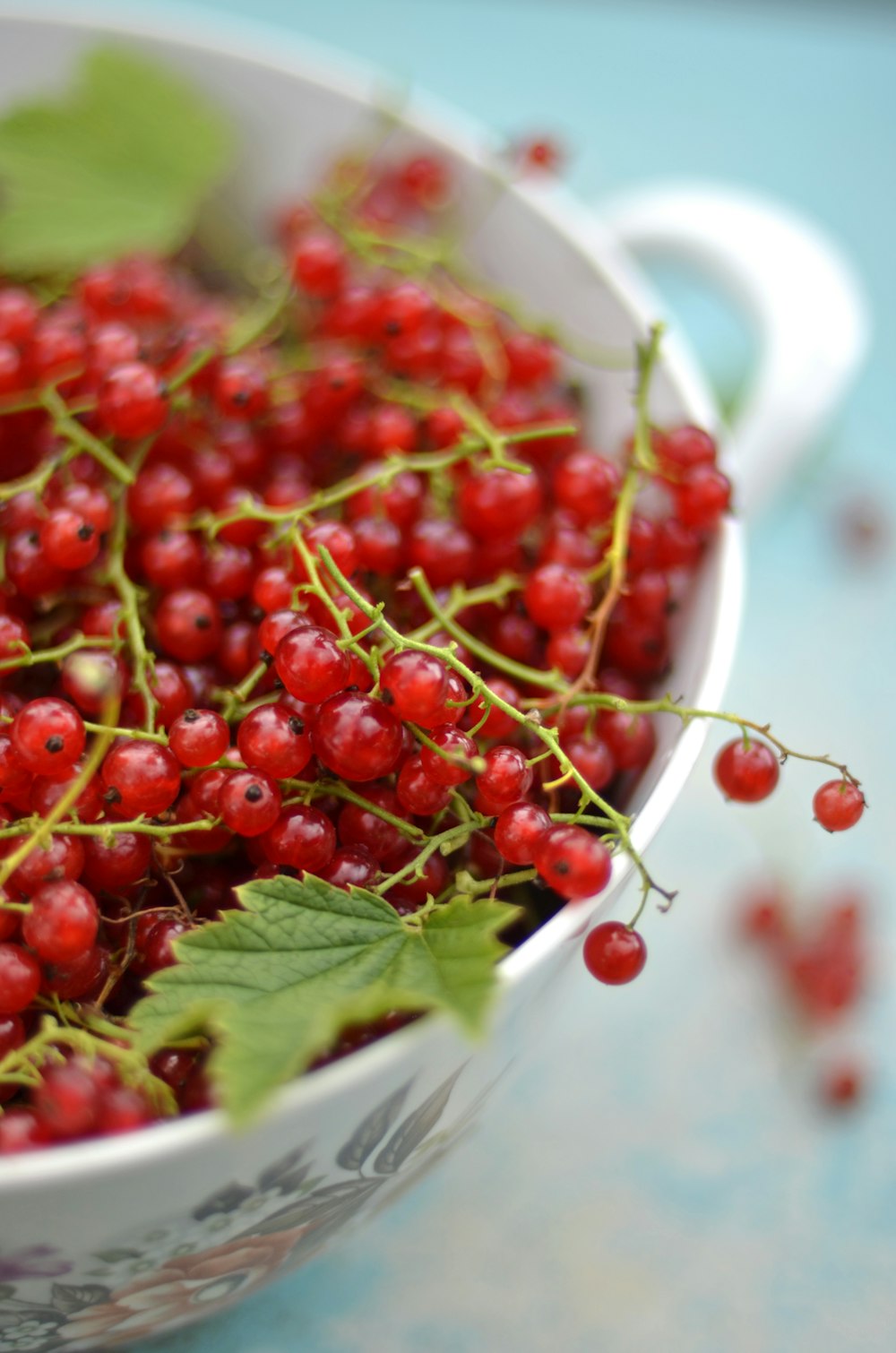 a white bowl filled with red berries and green leaves
