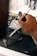 A person's hand is painting intricate floral designs on a gray drone. The background is blurred, with art supplies visible, including brushes and paint bottles.