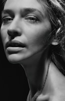 A monochrome portrait of a person with prominent facial features, including detailed eyes and textured skin. The lighting is dramatic, with strong contrasts highlighting the contours of the face and neck.
