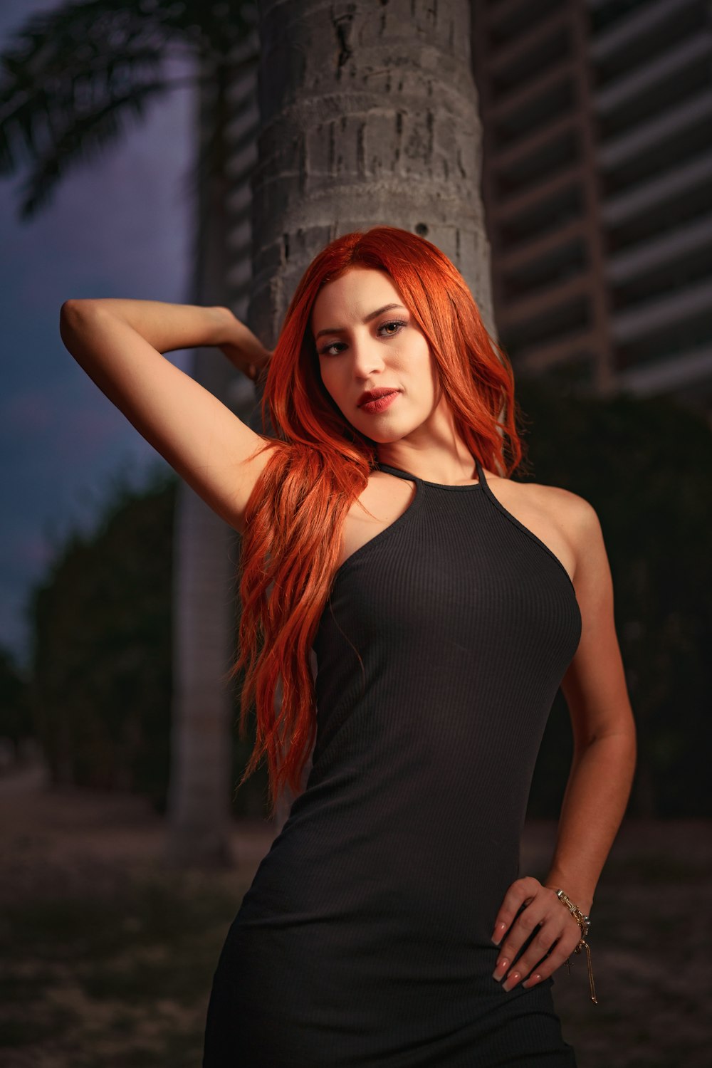a woman with long red hair standing next to a tree