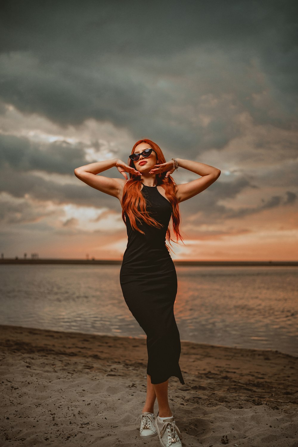 a woman in a black dress is standing on the beach