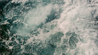 Turbulent ocean water churning with foam and bubbles, creating a dynamic and chaotic pattern of movement on the water's surface.