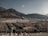 A vast array of white tents is spread across a large open area surrounded by mountainous terrain. Two minarets stand prominently in the foreground. The background consists of rugged hills under a clear sky, and there are several uniform, rectangular buildings at the base of the mountains.