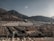 A vast array of white tents is spread across a large open area surrounded by mountainous terrain. Two minarets stand prominently in the foreground. The background consists of rugged hills under a clear sky, and there are several uniform, rectangular buildings at the base of the mountains.