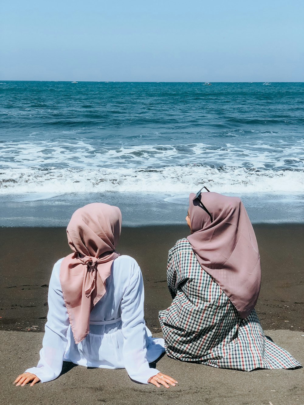 two women sitting on a beach facing the ocean