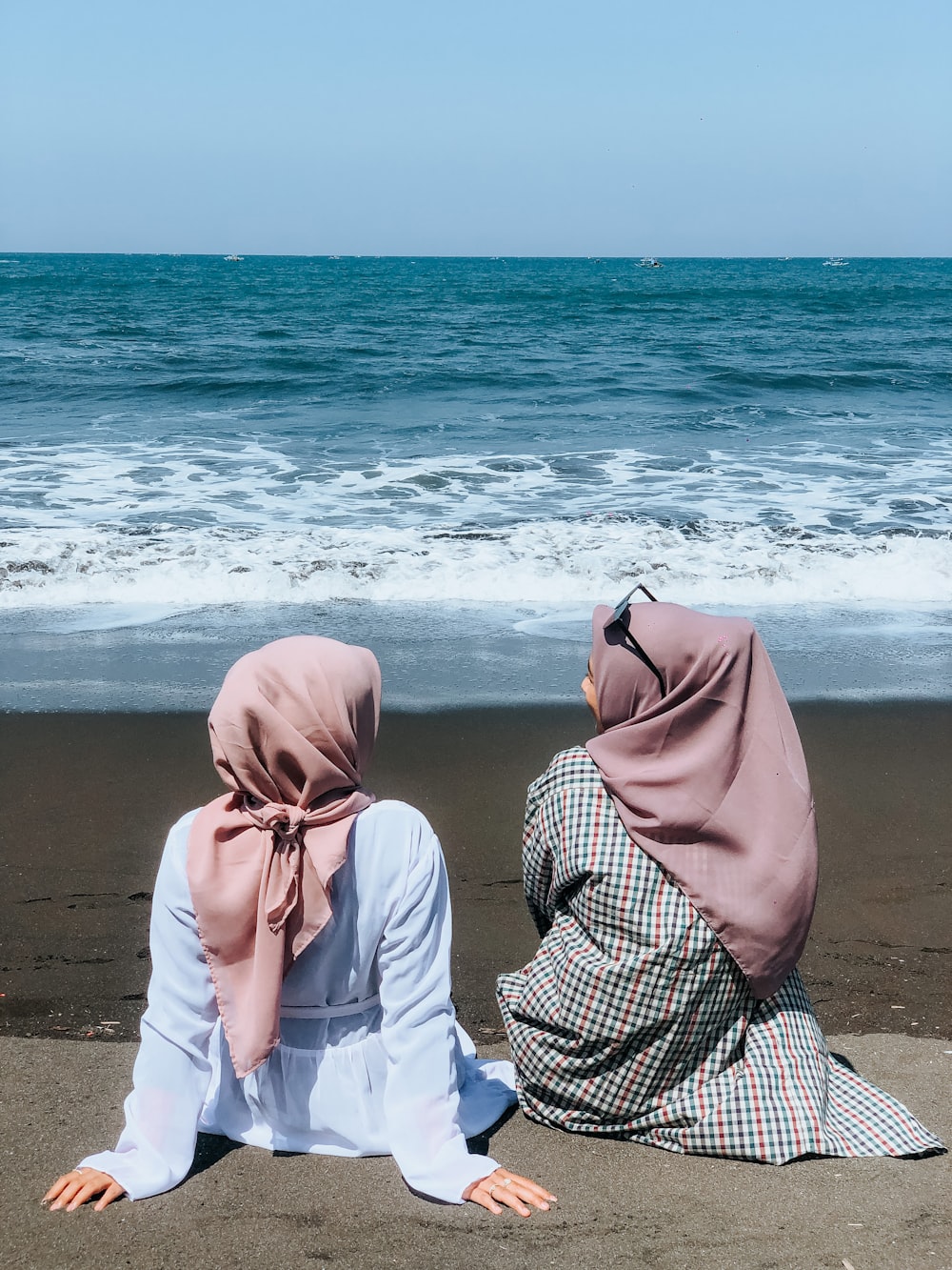 two women sitting on a beach facing the ocean