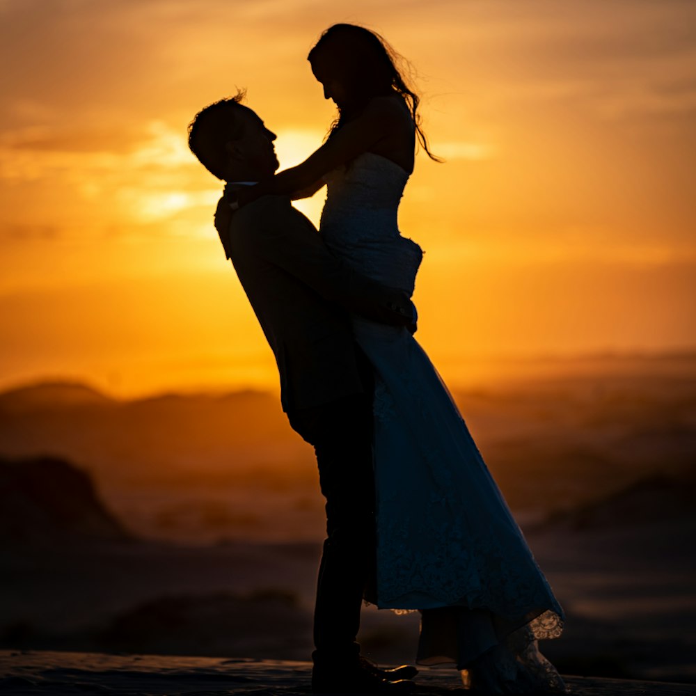 a bride and groom are silhouetted against a sunset