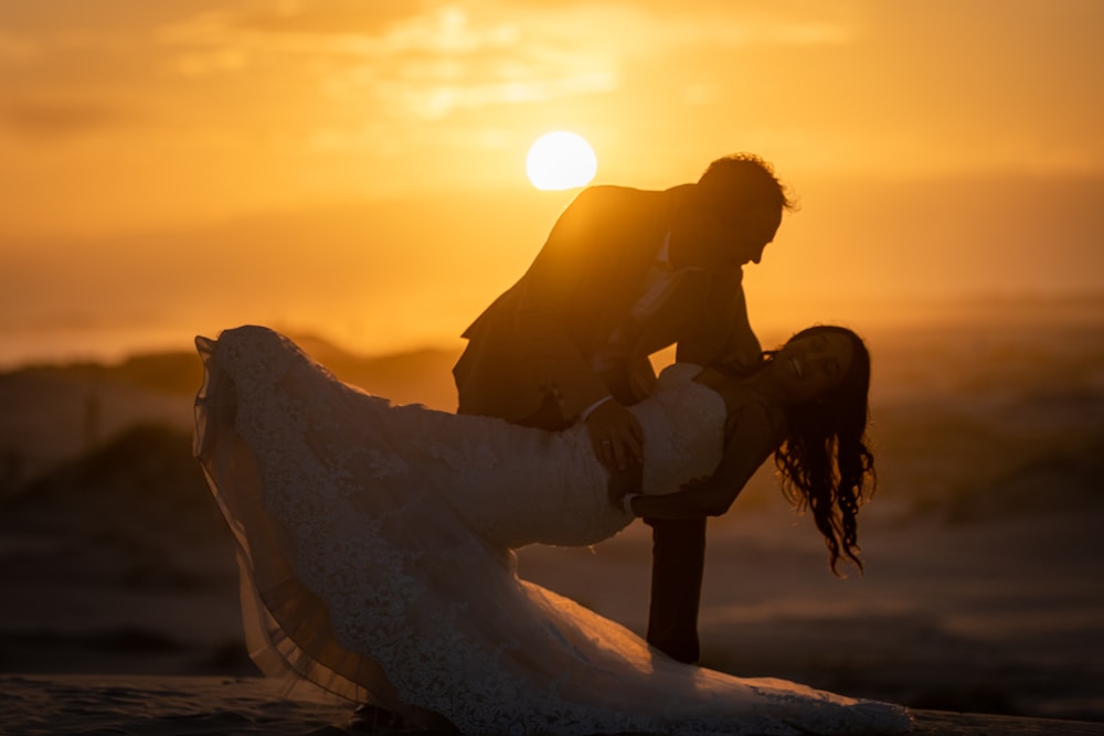 a bride and groom kissing on the beach at sunset