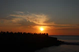 A group of divers silhouetted against a glowing sunset over the ocean horizon.
