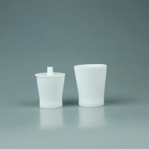 Two white, minimalist containers are placed side by side against a plain, light gray background. The container on the left includes a lid with a protruding spout, while the one on the right is taller and open at the top.
