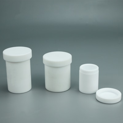 A set of three white, cylindrical containers with removable lids is displayed against a plain grey background. The containers vary in size, arranged from largest on the left to smallest on the right. The smallest container has its lid placed beside it.