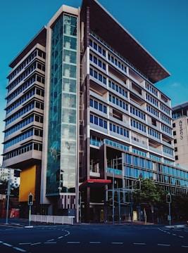 A modern multi-story office building with a sleek and architectural design featuring prominent glass facades and a unique angular rooftop. The structure has a combination of dark and light hues, with a significant glass entrance on the corner. Traffic lights and a city street are visible in the foreground.