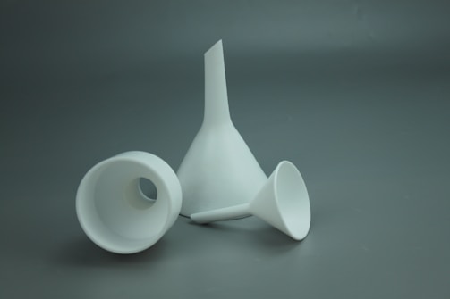 Three white funnels of varying sizes are placed on a gray surface. The largest funnel is upright, while the other two are placed horizontally.