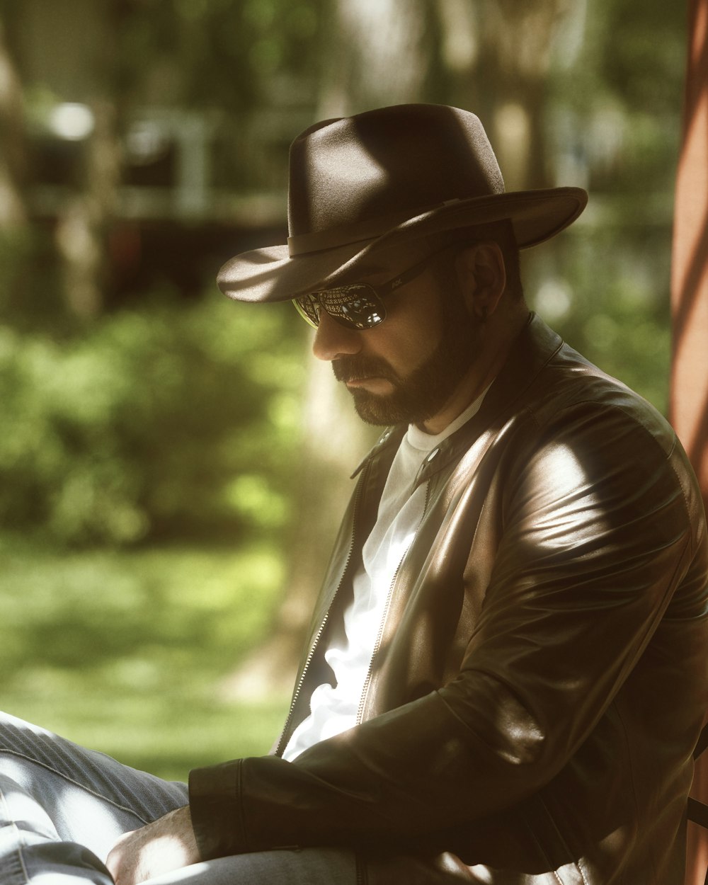 a man wearing a hat and glasses sitting on a bench