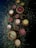 A collection of wooden bowls and containers filled with various powders and substances is arranged on a dark surface scattered with dried herbs. The bowls contain colorful powders including red, white, brown, yellow, and green hues.