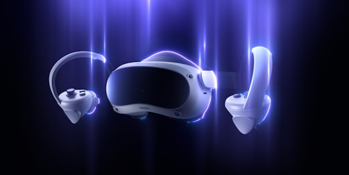 A futuristic virtual reality headset with two handheld controllers is featured against a dark background with a glowing blue aura surrounding them. The design is sleek and modern, emphasizing advanced technology.