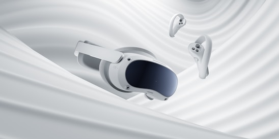 A virtual reality headset and two controllers are suspended against a backdrop of smooth, swirling white fabric, evoking a sense of fluidity and modern technology.