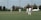 A well-maintained cricket turf with players warming up in the background
