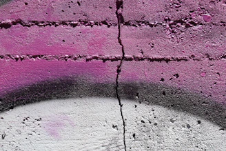 Close-up of textured concrete wall with graffiti art in muted tones blending black, gray, and burgundy accents.