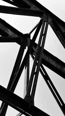 Black and white close-up of steel beams intersecting in an industrial warehouse.