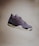 A single sneaker with a sleek, modern design is visibly suspended in mid-air against a plain background. The shoe features a mix of materials, including smooth leather and mesh, with intricate detailing around the lace area and a distinctive air cushion in the sole.