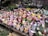 An assortment of small, decorative potted flower arrangements featuring a mix of colorful flowers including roses and daisies. The pots contain various decorative elements like artificial birds and small figurines. The scene is busy with a variety of colors and textures across the display.