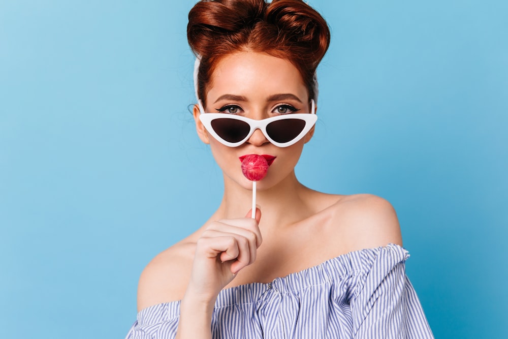 a woman wearing sunglasses holding a lollipop in front of her face