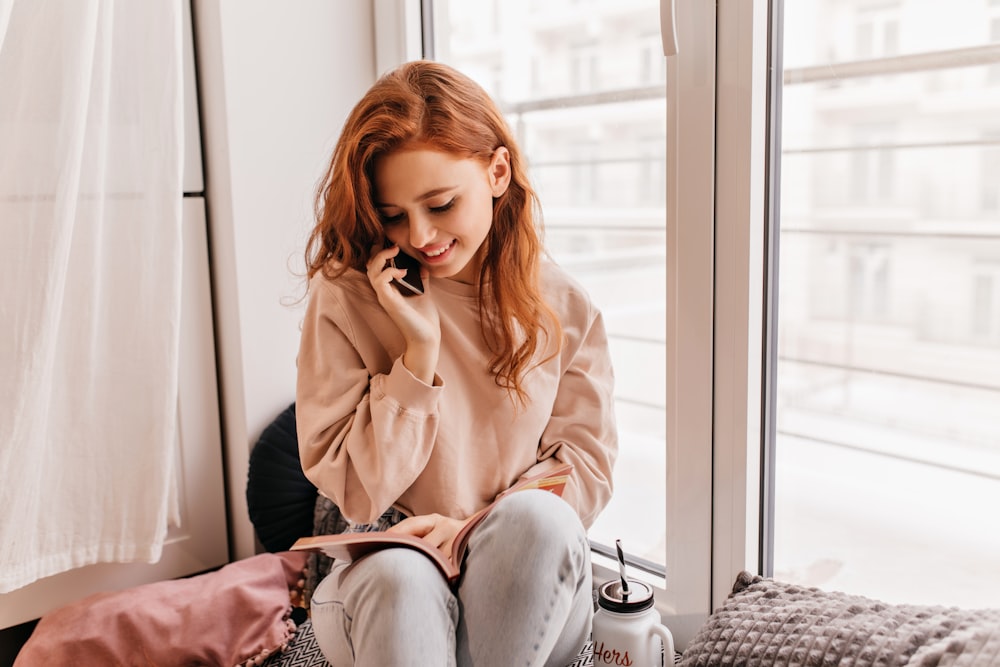 a woman sitting on a window sill talking on a cell phone