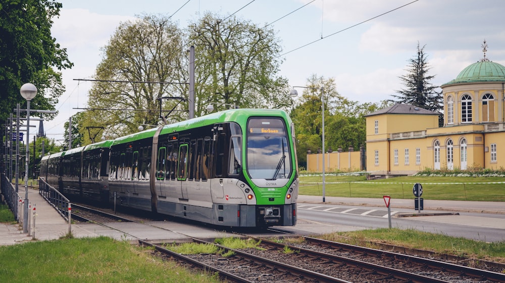 a green train traveling down train tracks next to a building