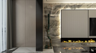 A modern, sleek interior with a vertical, ribbed panel integrated into a decorative wall. Beneath the panel, a linear gas fireplace emits artificial flames. The wall features a marble texture with a mix of dark and light tones. To the left, a section of softly pleated gray curtains is visible, adding an element of elegance.