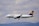 A commercial airplane in mid-flight with a clear view of its branding, flying against a background of cloudy skies and distant hills.