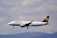 A commercial airplane in mid-flight with a clear view of its branding, flying against a background of cloudy skies and distant hills.
