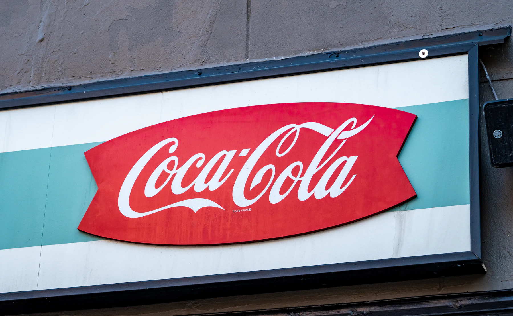 A red fishtail-shaped Coca-Cola sign on a white and green storefront panel