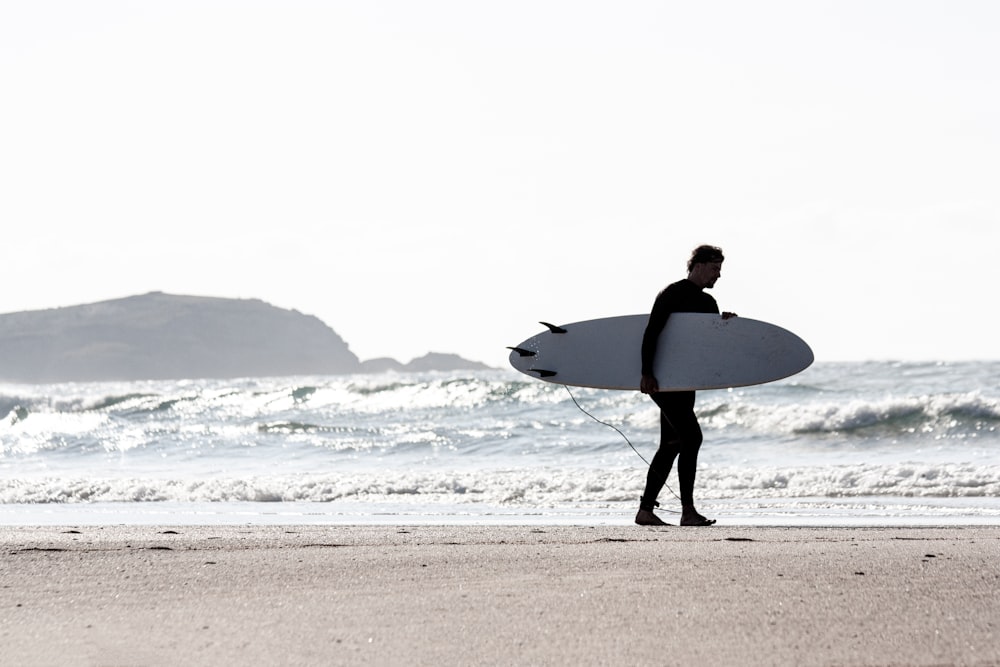 a man holding a surfboard on top of a sandy beach