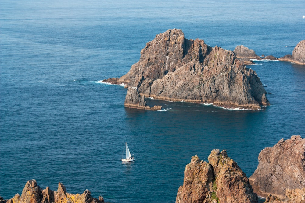 a sailboat in the ocean near some rocks