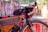 A close-up of a well-equipped bicycle is parked next to a colorful, graffiti-covered wall. The bike has several attached bags, including one on the frame and another on the handlebars. The handlebar has tape wrapped around it for grip, and the tire is a rugged, off-road type.