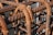 Rusted metal rebars intricately woven together, creating a grid-like structure. The metal displays signs of corrosion with brown rust overtaking the originally blue-gray surface. Sunlight casts shadows creating patterns and emphasizing the textured spirals on the bars.